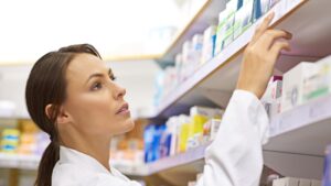 Woman serious and pharmacist on shelf at drug store for customer service and stock taking Female person inspection and check pills at pharmacy for packing medication and prescription at shop