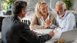 Happy senior woman encourages her husband to sign a contract with their bank manager during a meeting in the office