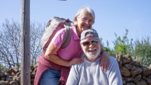 Cheerful caucasian senior couple looking at camera enjoying a mountain hike appreciating leisure