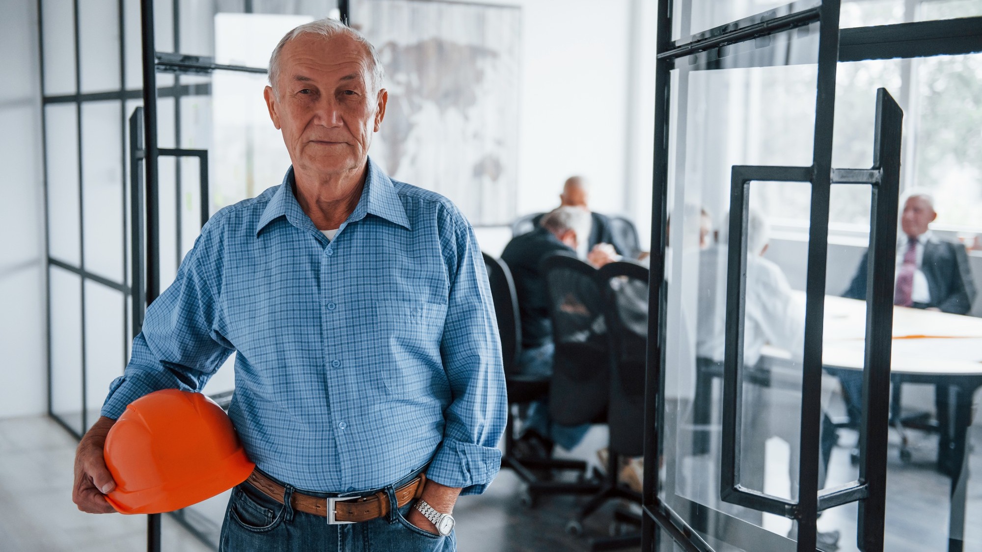 Portrait of senior man that stands in front of aged team of elderly businessman architects that have a meeting in the office.