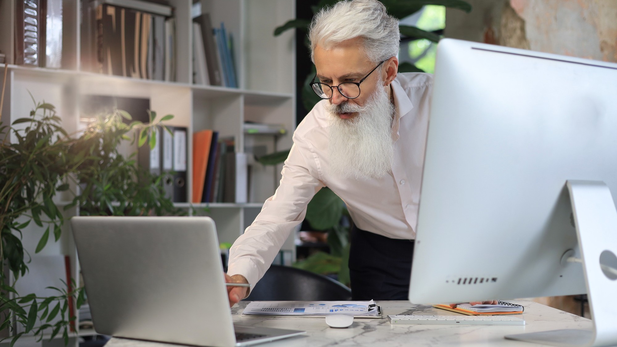 Senior businessman with a stylish beard working on laptop computer at his office desk.