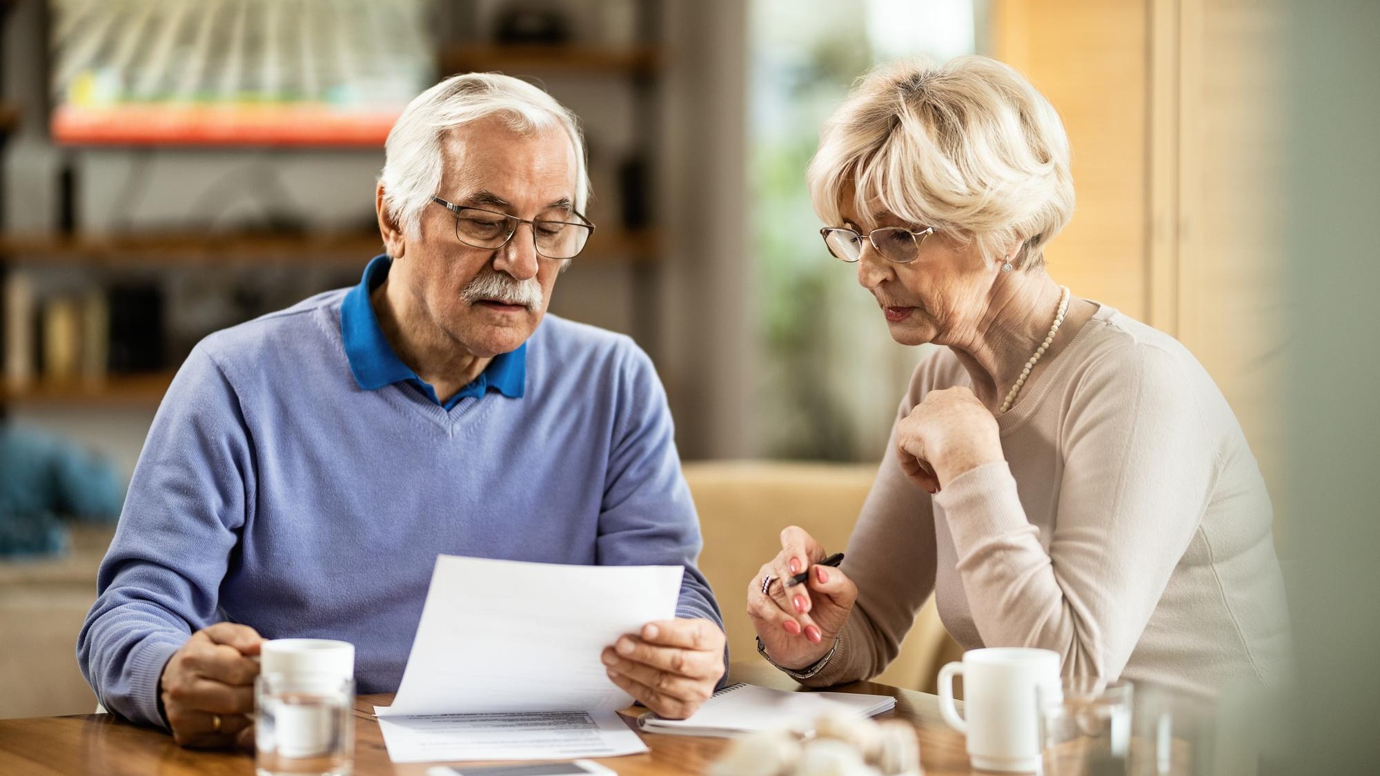 Senior man and his wife analyzing their savings while reading financial reports at home Senior man and his wife analyzing their savings while reading financial reports at home