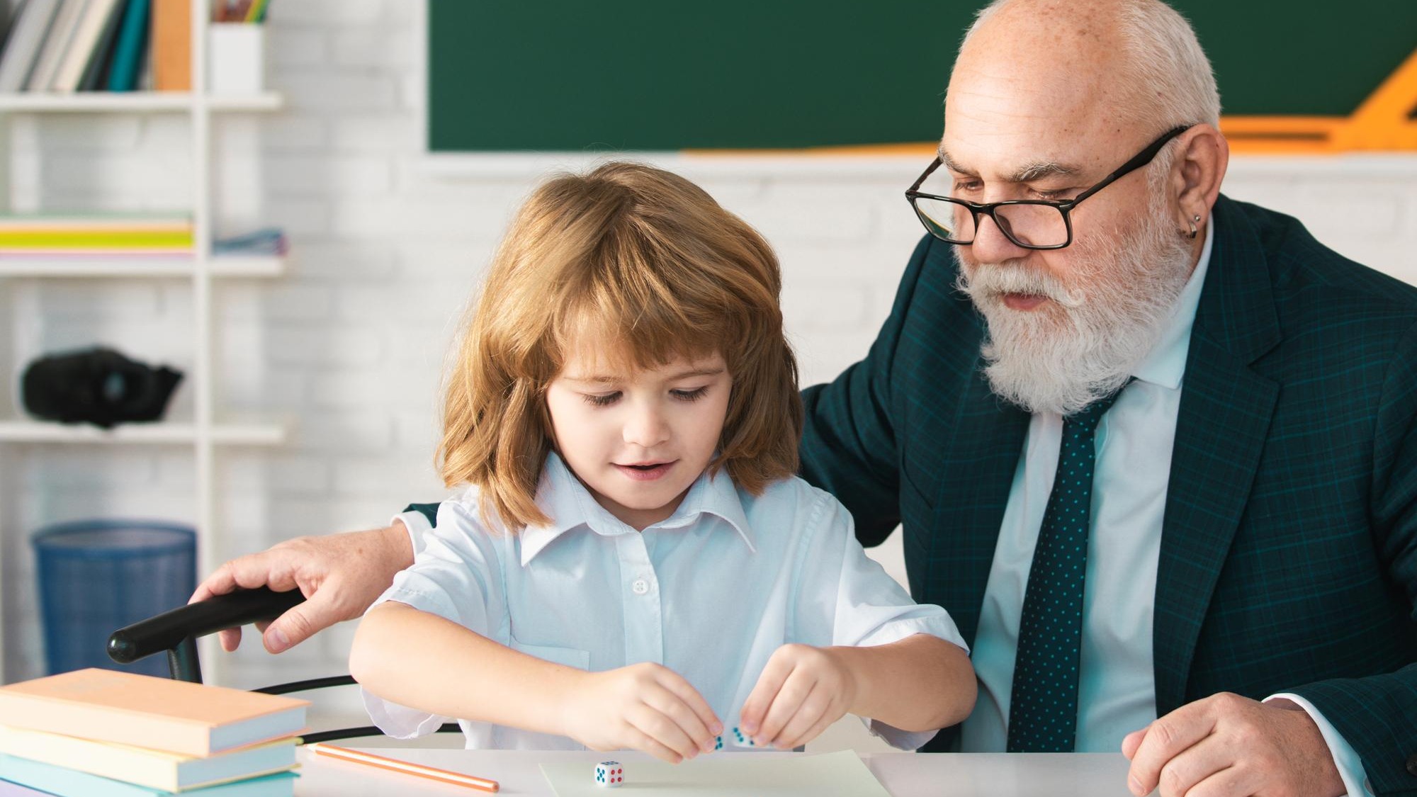 Senior teacher or grandfather and school boy pupil in classroom at school Private lesson Old tutor teacher help little boy pupil with studying math or language correct mistakes Senior teacher or grandfather and school boy pupil in classroom at school Private lesson Old tutor teacher help little boy pupil with studying math or language correct mistakes