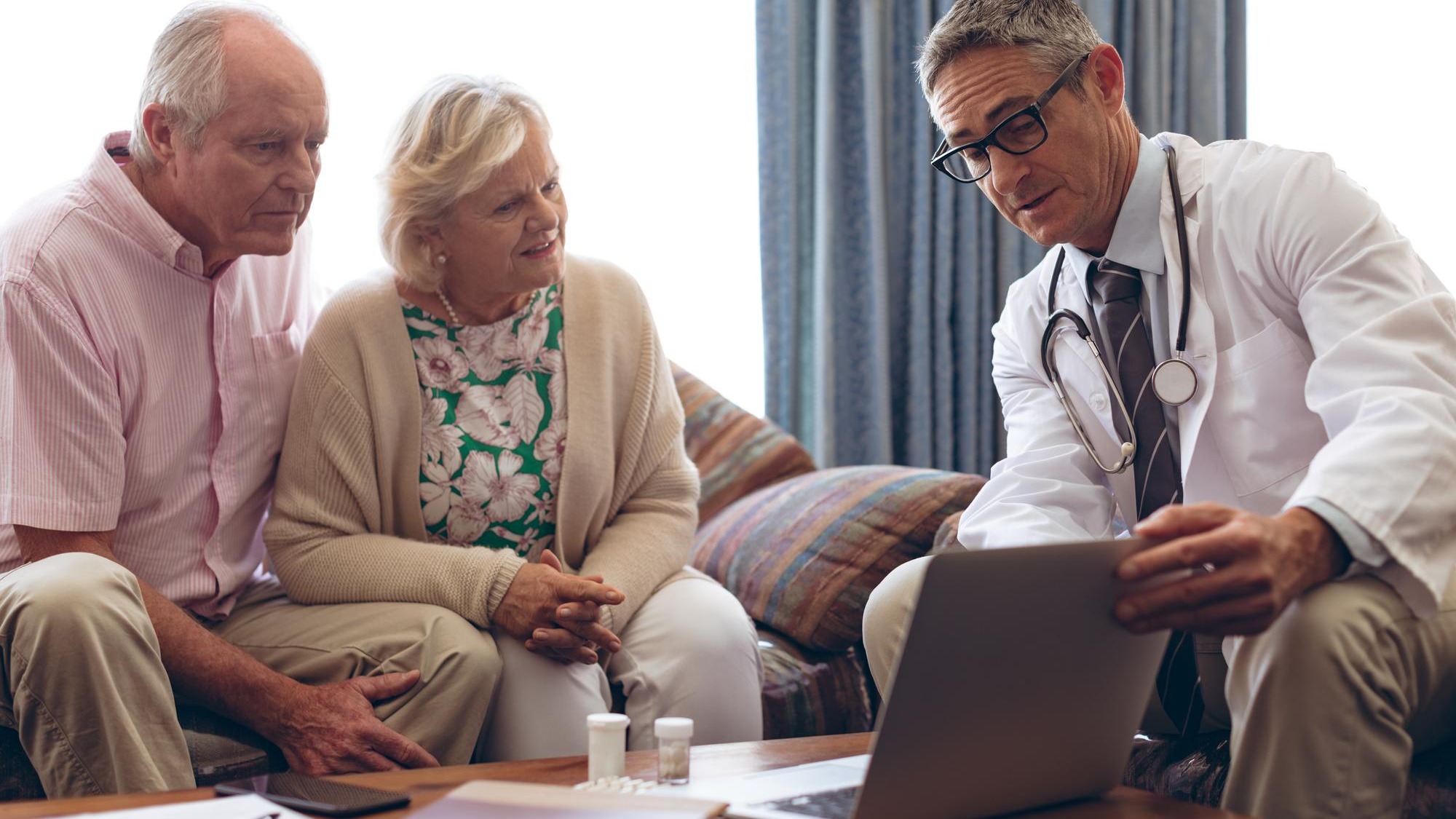 Male doctor discussing over laptop with senior couple at retirement home