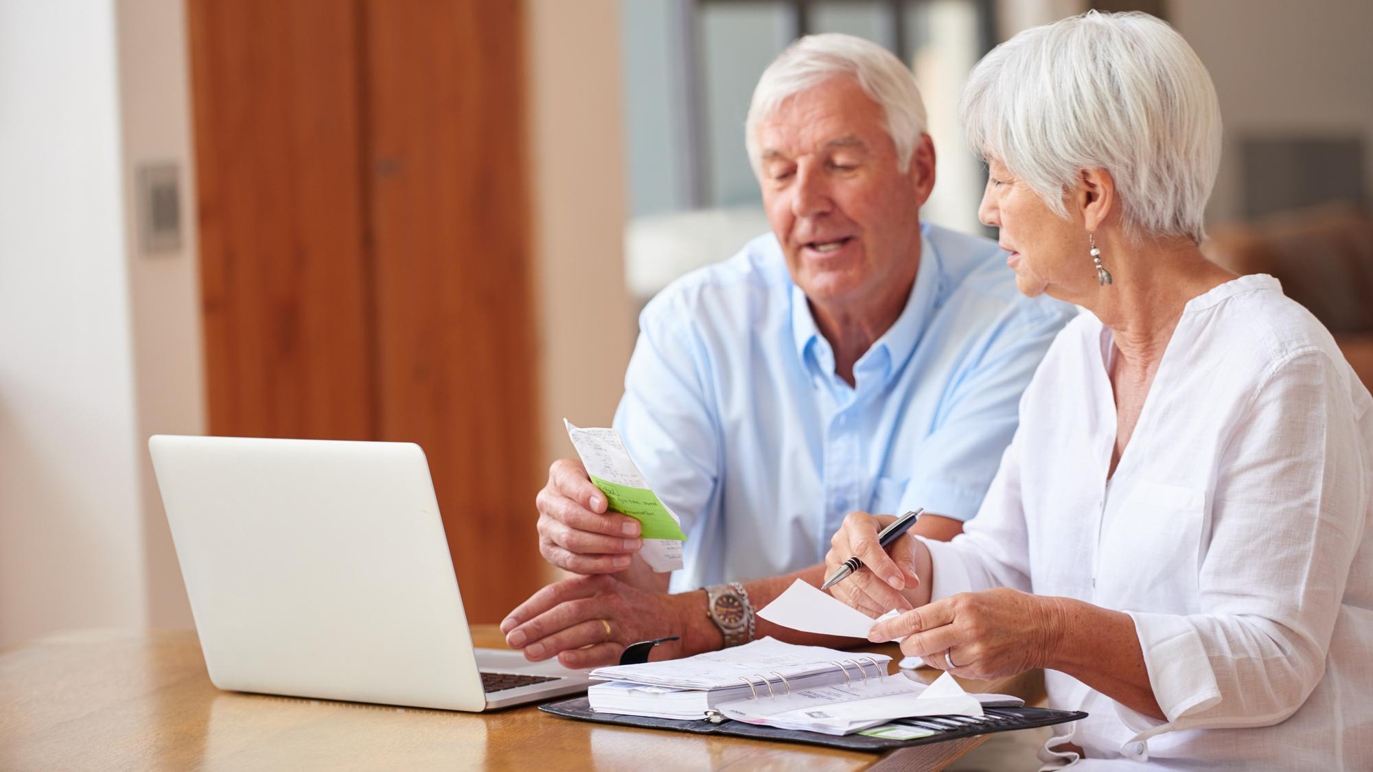 Old couple talking and laptop in home with documents utility bills review and financial planning Married elderly people and computer with paperwork for household costs budget and communication