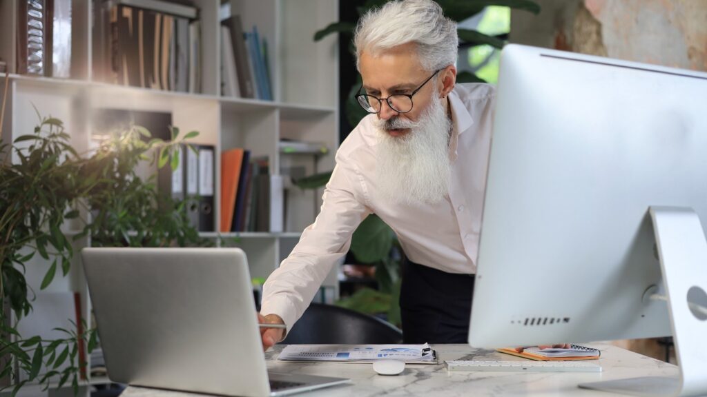 Senior businessman with a stylish beard working on laptop computer at his office desk.