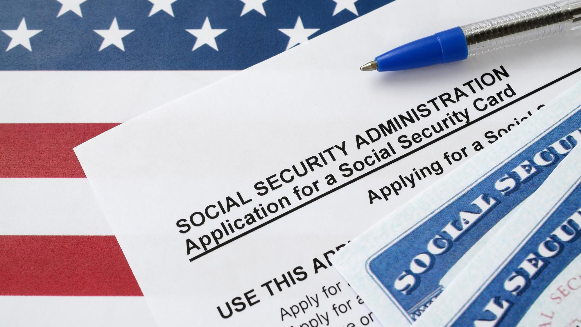 United States social security number cards lies on Application from social security administration with blue pen on US flag United States social security number cards lies on Application from social security administration with blue pen on US flag
