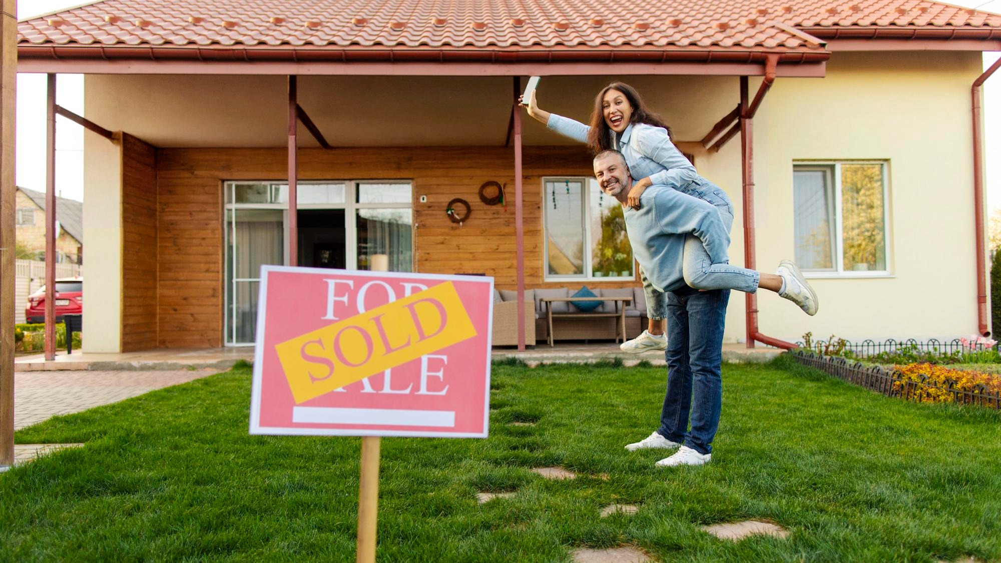 Excited couple new homeowners posing in front of their house having fun man piggybacking wife sold Excited couple new homeowners posing in front of their house having fun man piggybacking wife sold