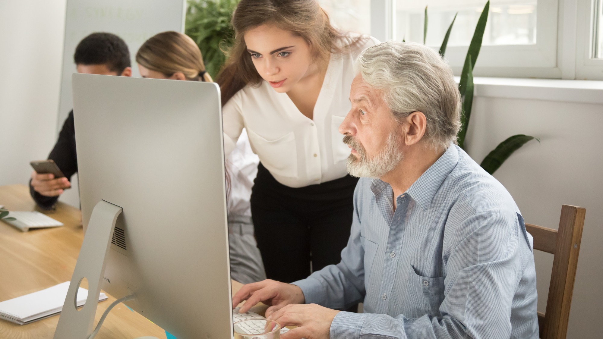 Female executive teaching senior office worker helping explaining computer work Female executive teaching senior office worker helping explaining computer work